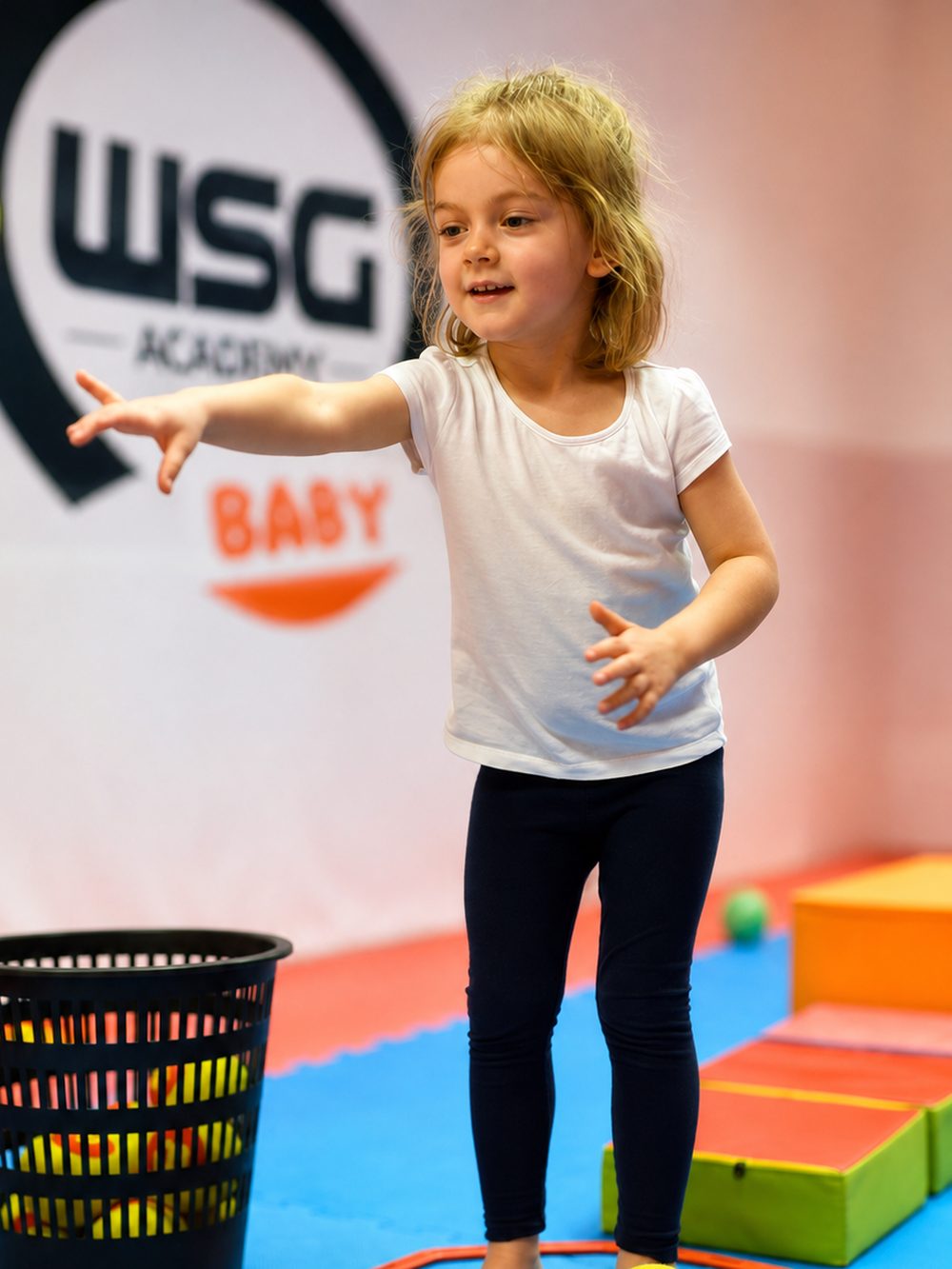 Dziewczynka rzuca piłką do kosza na zajęciach WSG Academy Baby